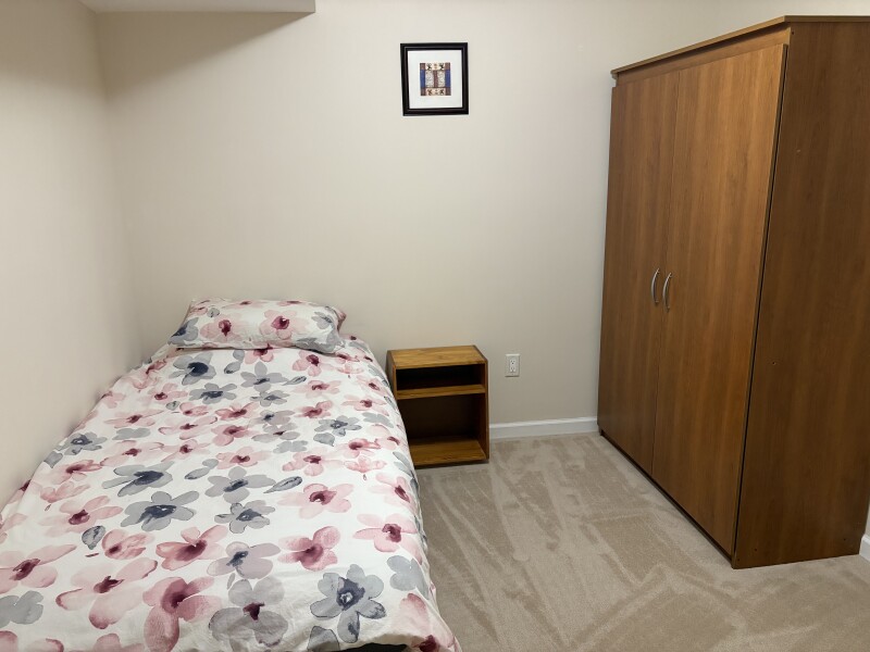Furnished bedroom with bathroom next door. Includes a closet, desk, bed, bedside table and bedding. 